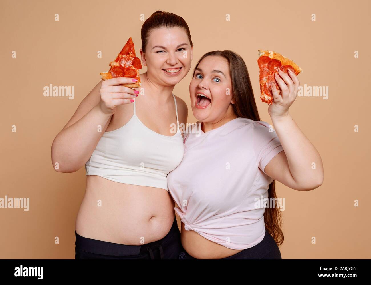 Mädchen essen Pizza auf beigefarbenem Hintergrund. Überessen und Bauchfett Stockfoto