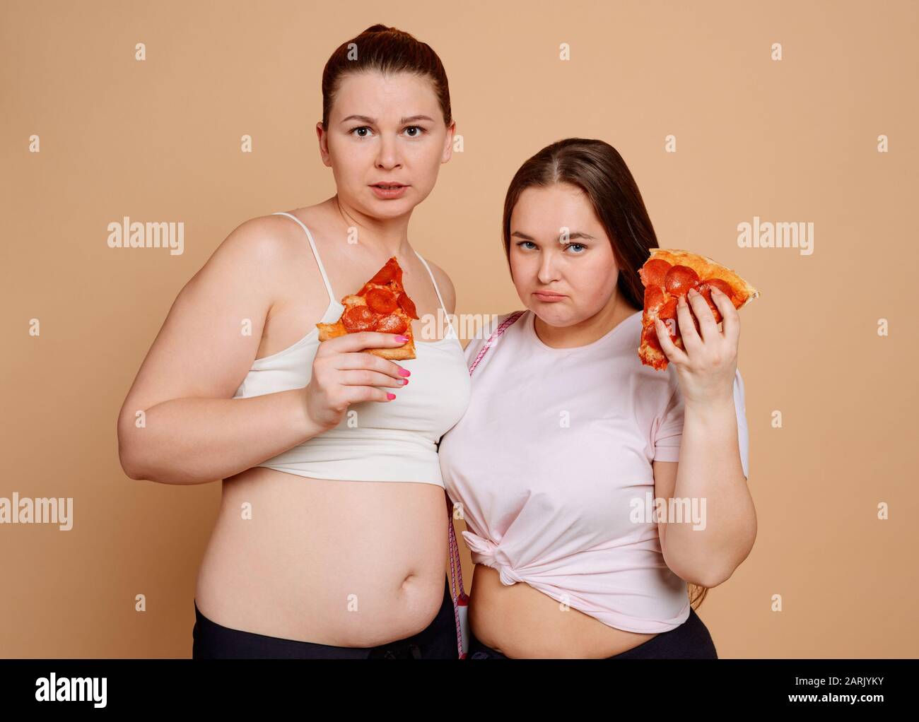 Frauen, die Pizzascheiben halten und versuchen, mit dem Überessen aufzuhören Stockfoto