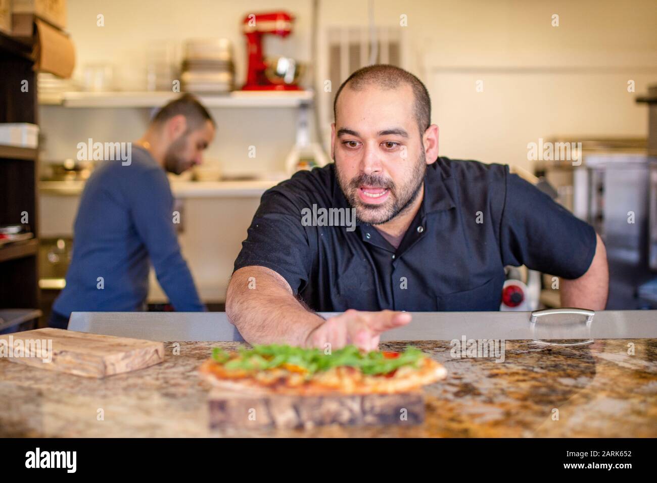 Ein Koch lehnt sich über eine Küchentheke und beschreibt ein zubereitetes Gericht Stockfoto