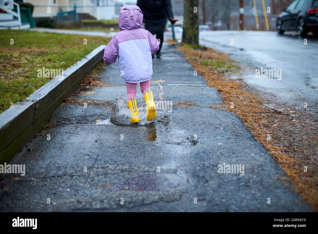 Ein kleines Mädchen, das Spaß hat, an einem regnerischen Tag in Pfützen zu planschen. Stockfoto