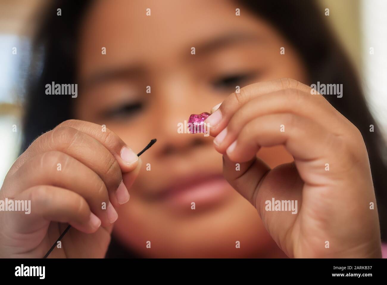Ein kleines Mädchen, das die visuellen motorischen Fähigkeiten oder die Hand- und Augenkoordination beim Einfädeln von Perlen verbessert. Stockfoto