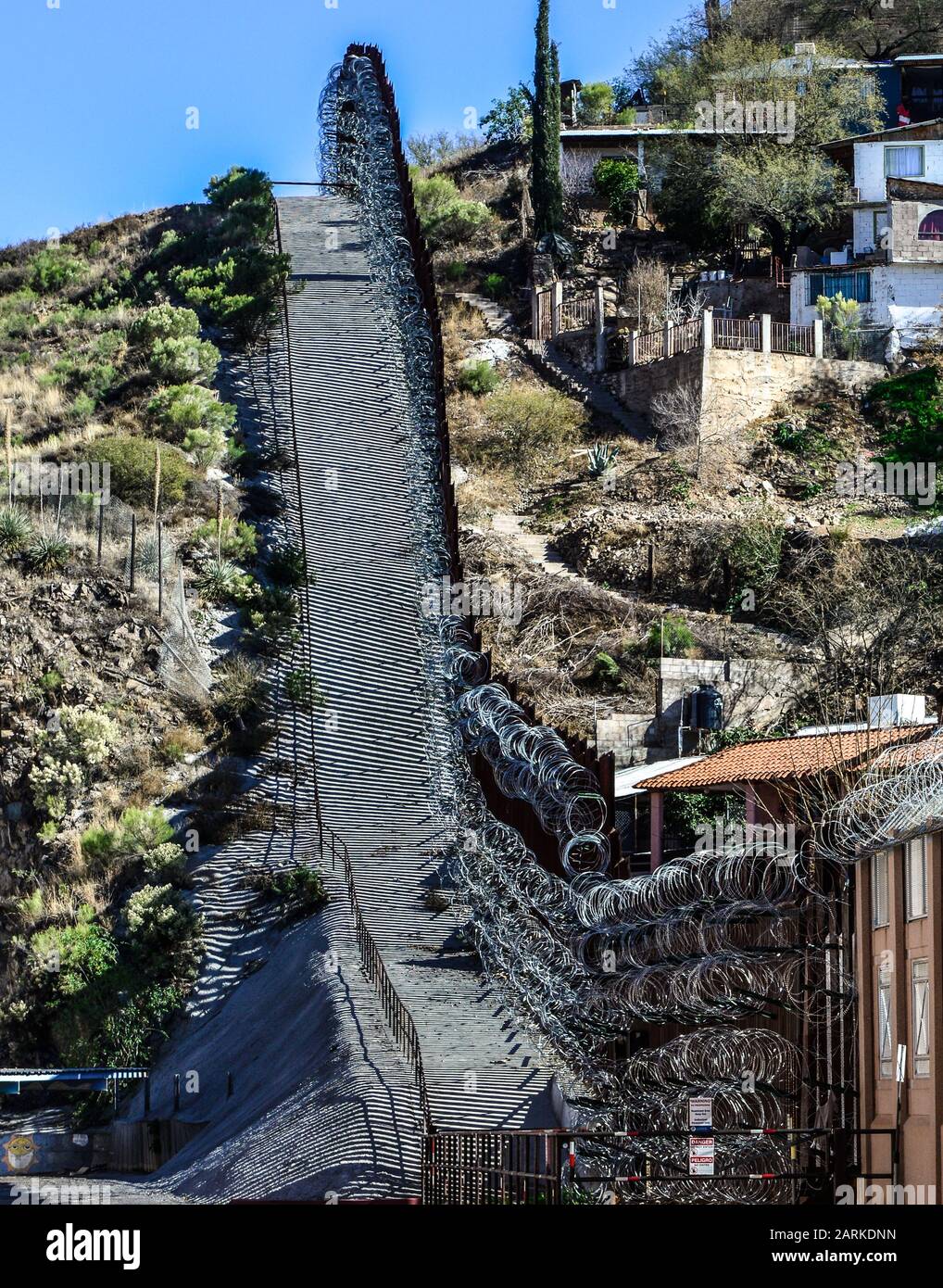 Blick auf den internationalen Grenzzaun aus US/Mexiko mit Rasierdraht, der sich bergauf mit mexikanischen Häusern auf der anderen Seite des Zauns von Nogales, AZ, USA, befindet Stockfoto