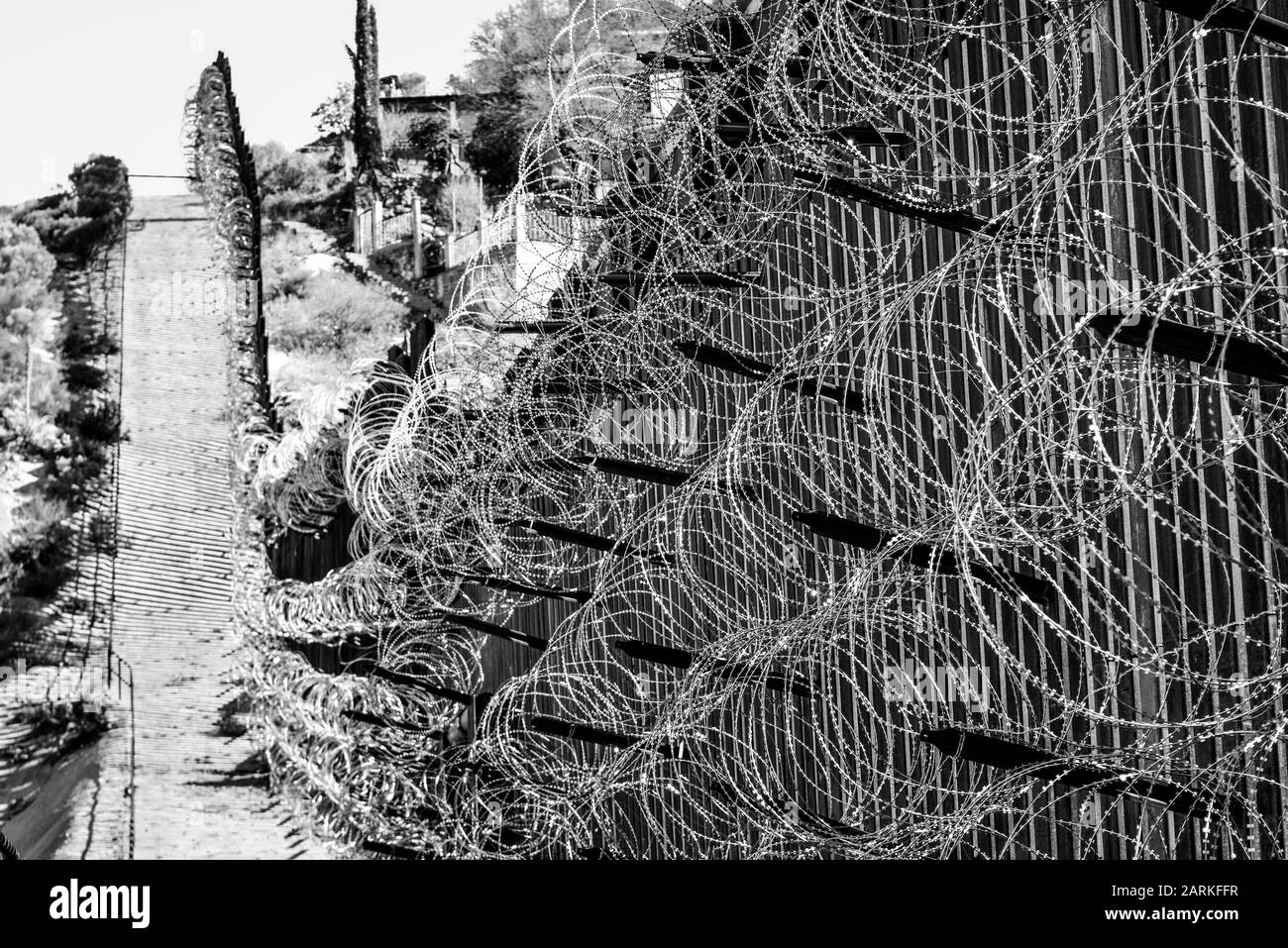 Nahaufnahme des internationalen Grenzzauns USA/Mexiko mit Rasierdraht nach bergauf mit mexikanischen Häusern auf der anderen Seite des Zauns von Nogales, AZ, USA, i. Stockfoto