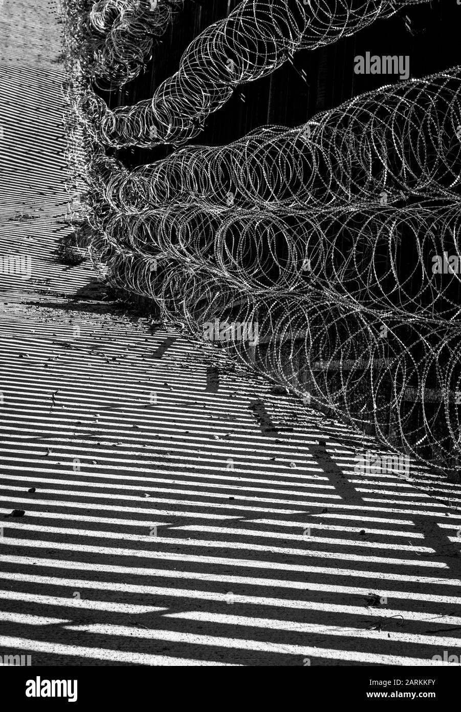 Abstrakte Ansicht des internationalen Grenzzauns USA/Mexiko mit Rasierdraht mit dramatischem Licht und Schatten in Nogales, AZ, USA, in Schwarzweiß Stockfoto