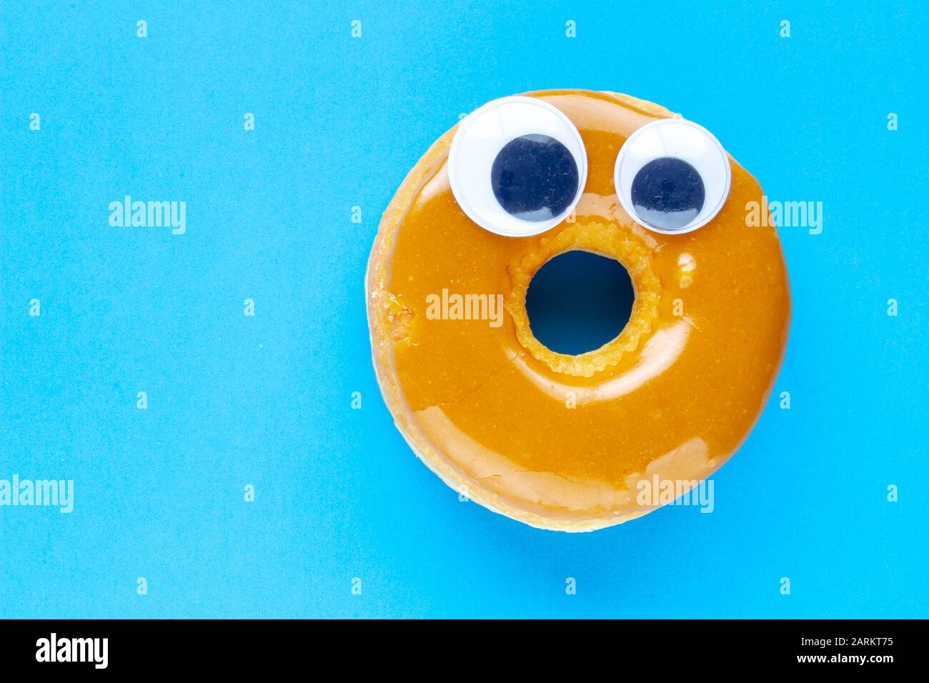 Ein kanadischer Maple Dip Donut mit Black Wiggle Googly Augballs auf blauem Hintergrund Stockfoto
