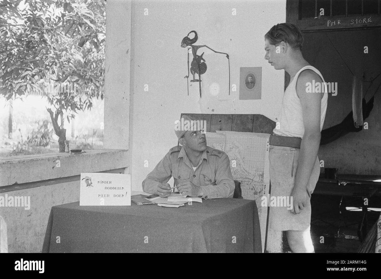 Tangerang Ensign? Saß am Tisch mit einem Schild mit dem Bild von Donald Duck und dem Text "weniger Klatsch, mehr tun" Datum: Juli 1947 Ort: Indonesien, Niederländische Ostindien, Tangerang Stockfoto