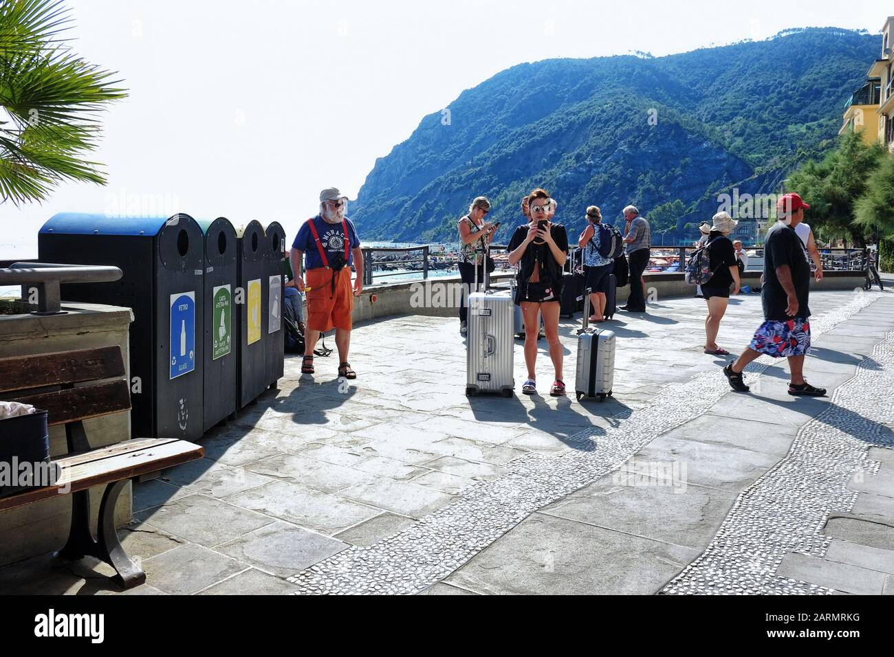 Frau, die in Monterosso Cinque Terre ankommt, mit zwei Koffern Reisegepäck, die auf der Promenade stehen und ihr Telefon an der italienischen Riviera abfragen Stockfoto