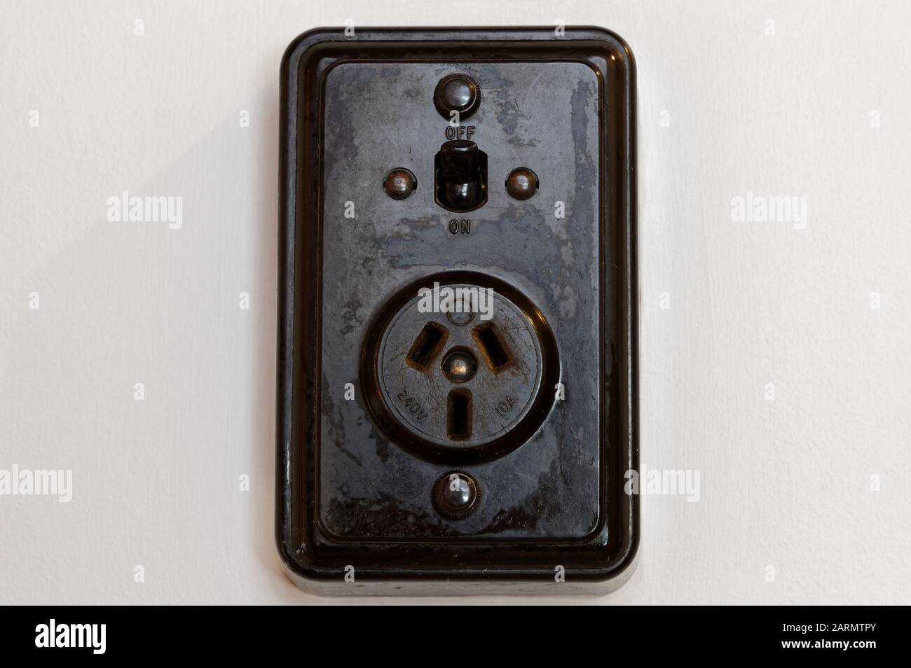Eine schwarze Bakelitsteckdose mit neuseeländischem Stecker ist an einer weißen Wand montiert Stockfoto