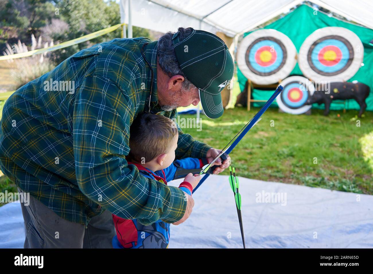 Ein Junge im Spiderman Outfit hält Bogen und Pfeil, als ein erwachsener Mann ihm beibringt, auf dem Steelhead Festival am Lake Sonoma California auf Ziele zu schießen. Stockfoto