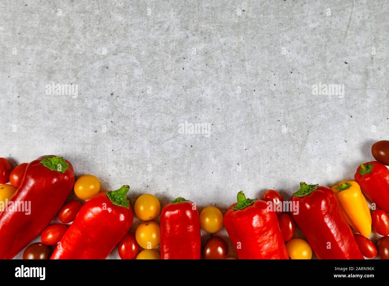 Chili-förmige rote Paprika und kleine gelbe und rote Tomatengemüse auf der Unterseite mit leerem Kopierraum im Hintergrund oben Stockfoto