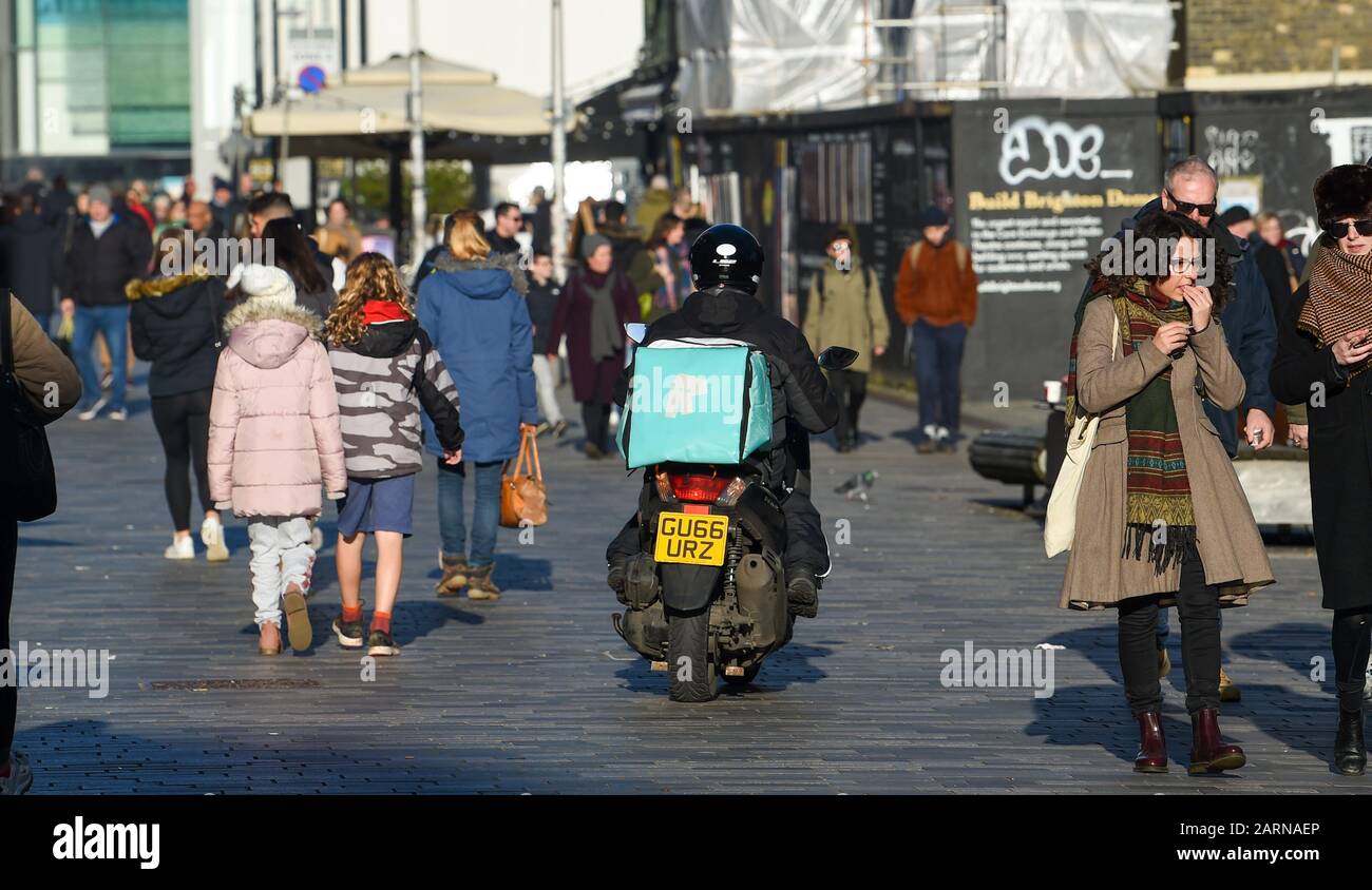 Ein Fahrer von Deliveroo auf einem Roller webt unter Fußgängern in Brighton Stockfoto