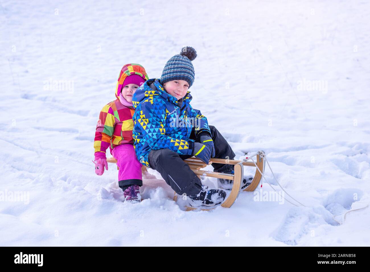 Mädchen und Junge auf Schlitten. Bruder und Schwester im Winter Kleidung mit Jacke, Kappe und Handschuhen. Stockfoto