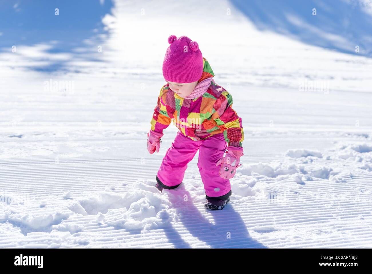 Kleines Mädchen spielt im Schnee. Mädchen tragen einen rosafarbenen Hut, einen Schal, eine Jacke, Handschuhe und einen Anzug. Konzept Winterurlaub Stockfoto