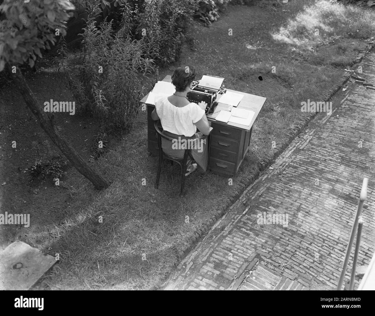 Heat Wave Lady mit Schreibtisch und Maschine im kühlen Garten Datum: 23. August 1955 Schlagwörter: Damen, Maschinen, Gärten Stockfoto