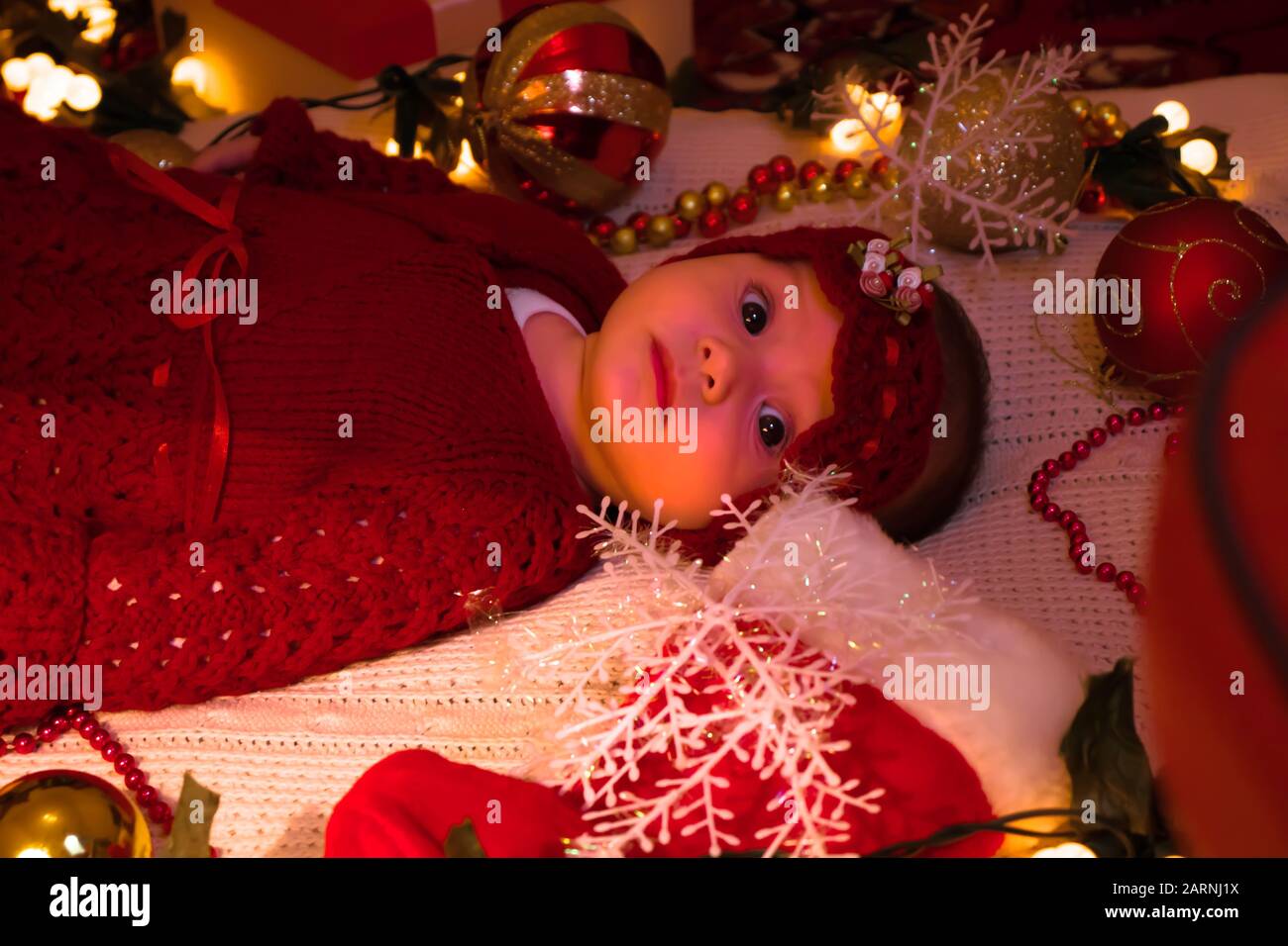 Ein süßes Mädchen in einem roten Outfit auf einer weißen Decke am Heiligabend. Stockfoto