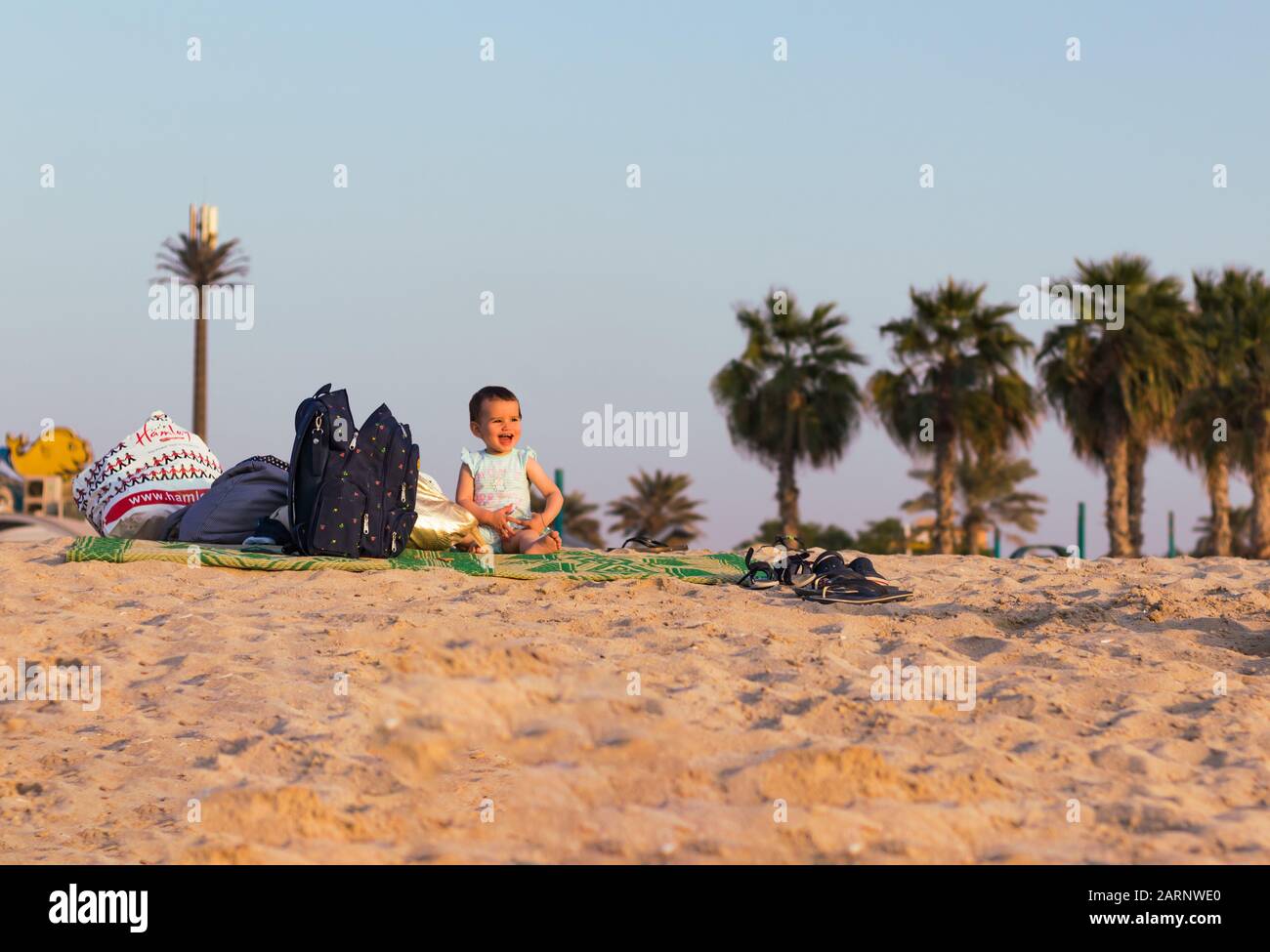 Porträt eines glücklichen kleinen Mädchens am Meer in Dubai mit Palmen und blauem Himmel im Hintergrund. Stockfoto