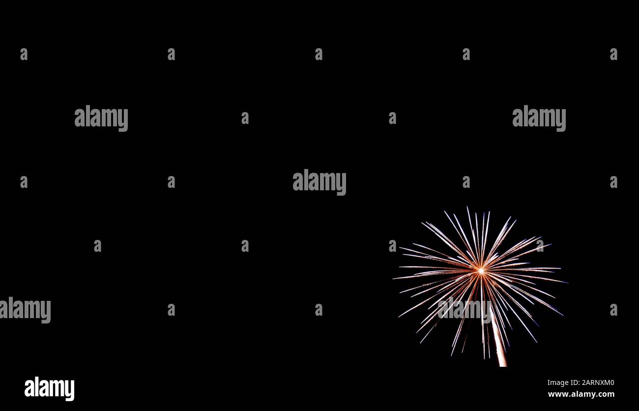 Kleines weißes Starburst-Feuerwerk in der rechten unteren Ecke, das am vierten Juli in Minnesota gegen einen schwarzen Himmel fotografiert wurde Stockfoto