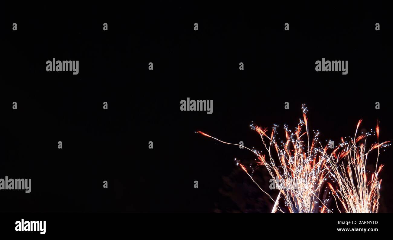 Rot-goldenes strömendes weizenförmiges Feuerwerk mit weißen Akzenten, das am vierten Juli in Minnesota gegen einen schwarzen Himmel fotografiert wurde Stockfoto