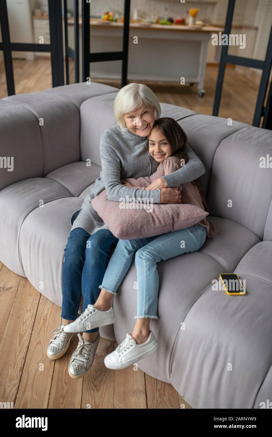 Großmutter und Enkelin sitzen umarmend auf einem Sofa. Stockfoto
