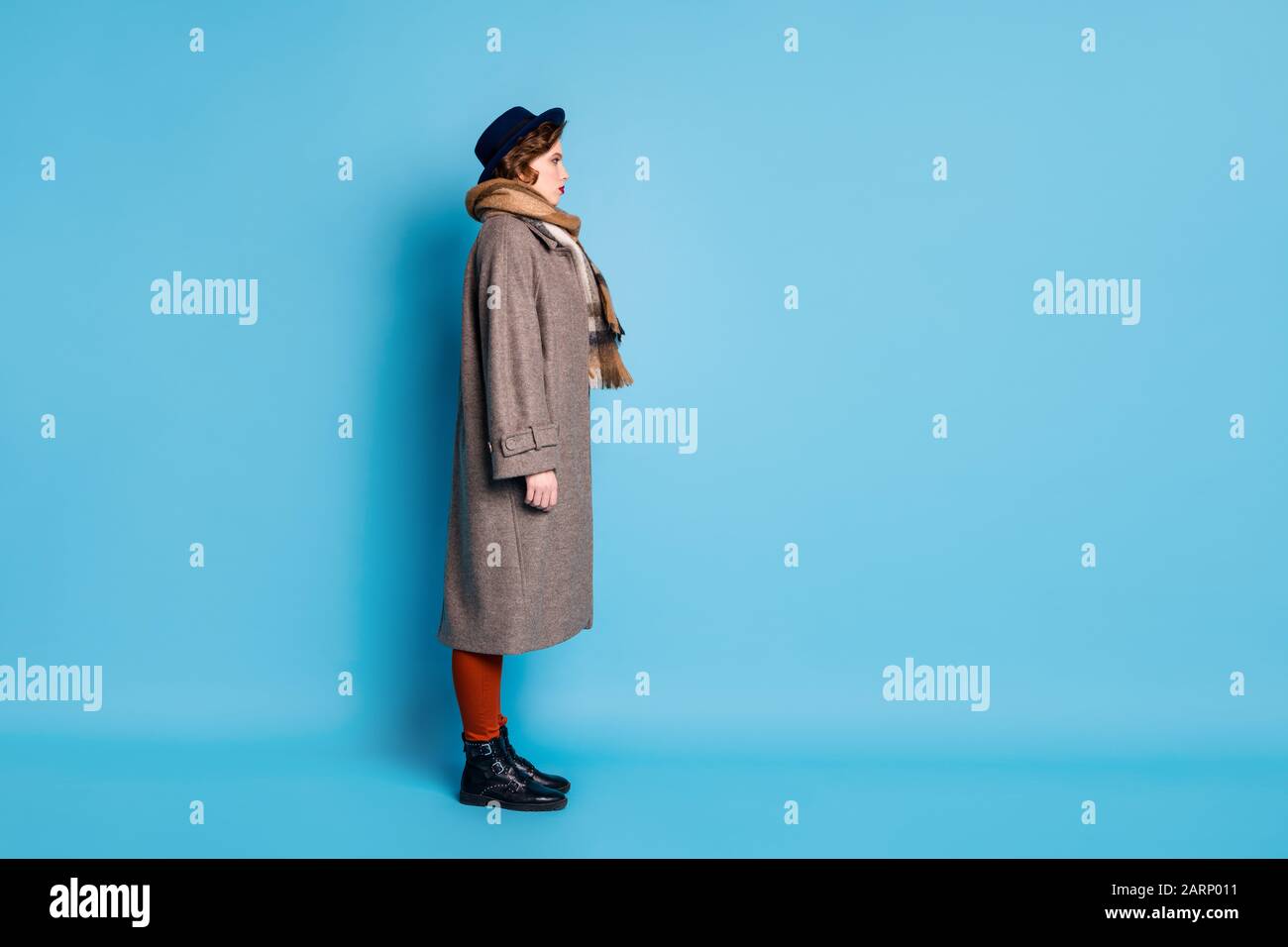 Lange Profilbild der hübschen Reisenden Dame, die an der Bushaltestelle steht, wartet auf Ankunft tragen Sie stylische Freizeit lang grau Mantel Schal Hosen Hut Schuhe Stockfoto