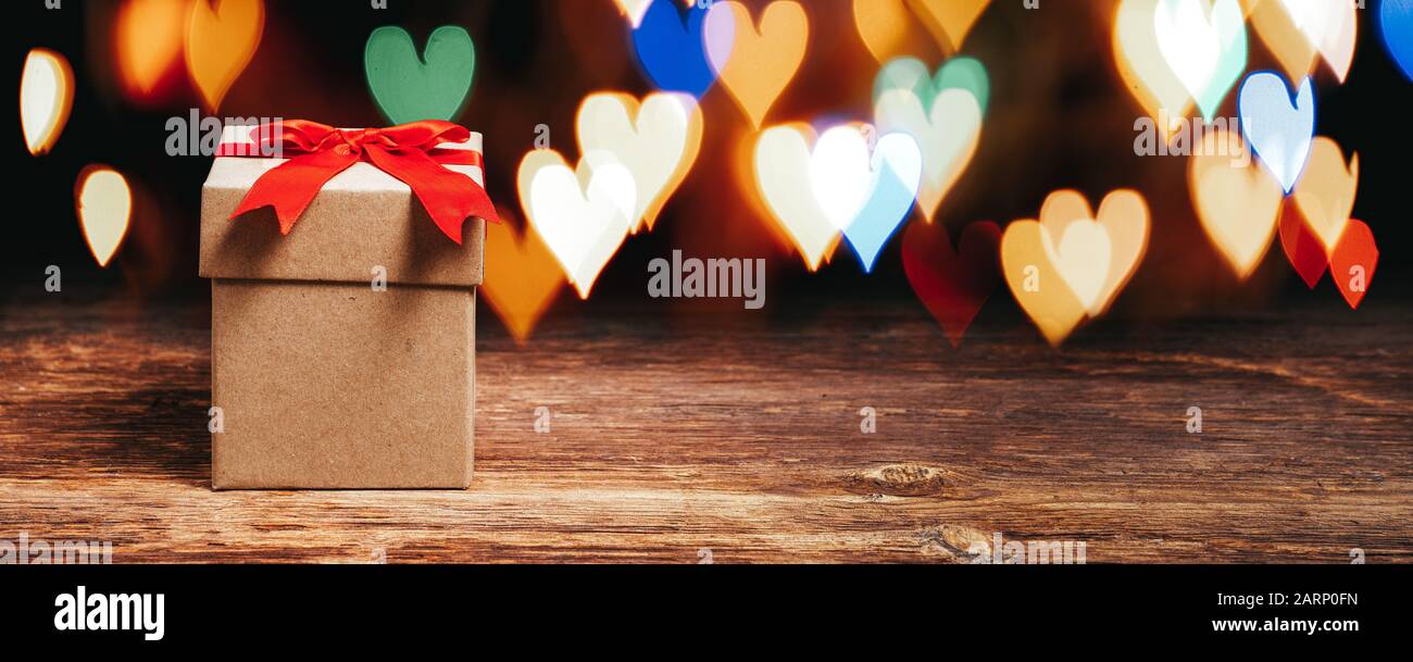 Geschenkbox auf Holztisch mit glänzenden, herzförmigen Lichtern Stockfoto