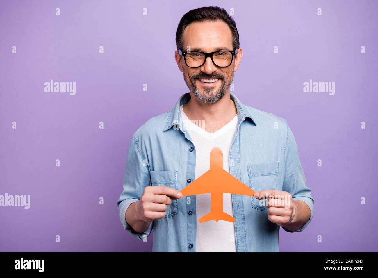 Portrait des positiven fröhlichen Mannes hält orangefarbenes Papierkarten-Flugzeug Want Go Abroad Reise an Sommerferien tragen Lifestyle-Kleidung isoliert Stockfoto