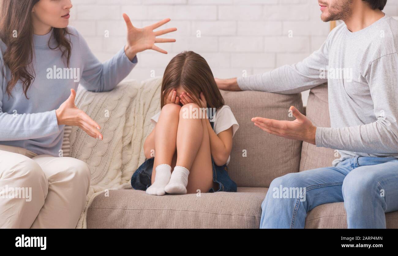 Unschuldiges kleines Mädchen, das zwischen streitenden Eltern sitzt und weint Stockfoto