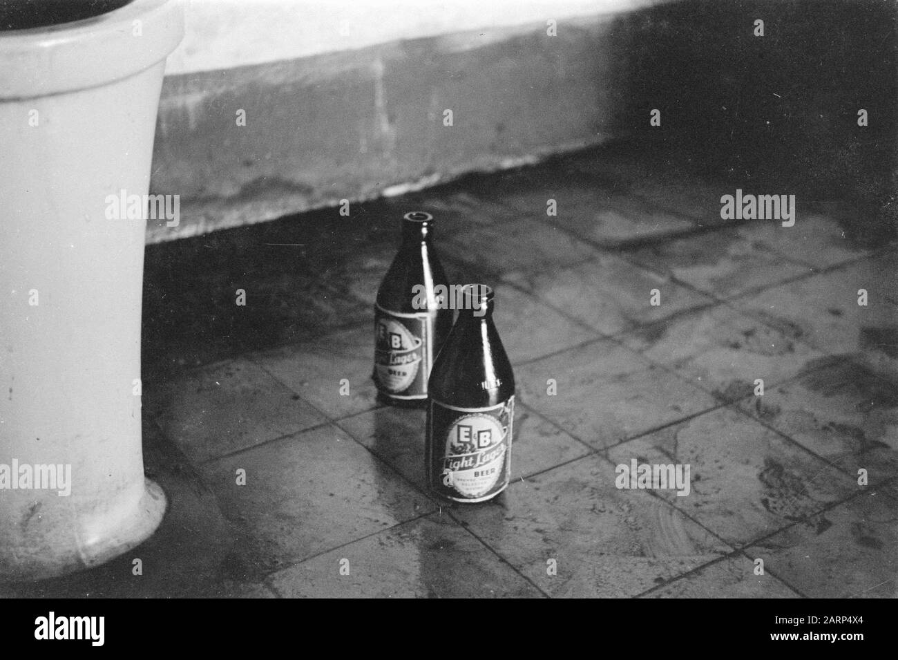 Zwei Flaschen Bier auf einem gefliesten Boden in der Nähe eines Toitletpots Anmerkung: Marke: E&B Light Lager Bier Datum: 1947/01/01 Ort: Indonesien, Niederländische Ostindien Stockfoto