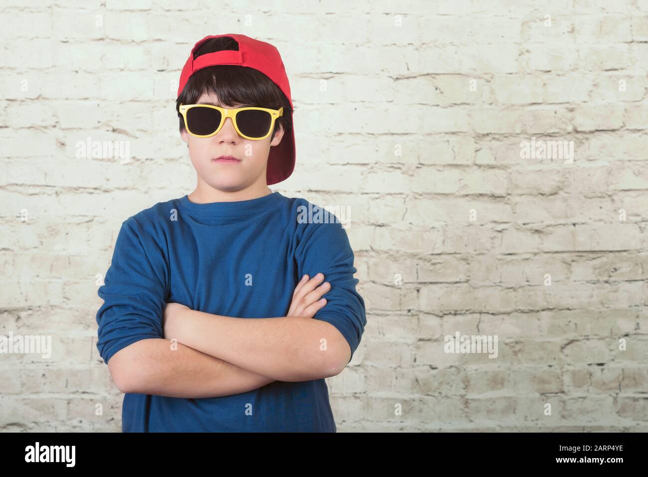 Verärgerter Junge mit Sonnenbrille und Kappe vor Backstein-Hintergrund Stockfoto