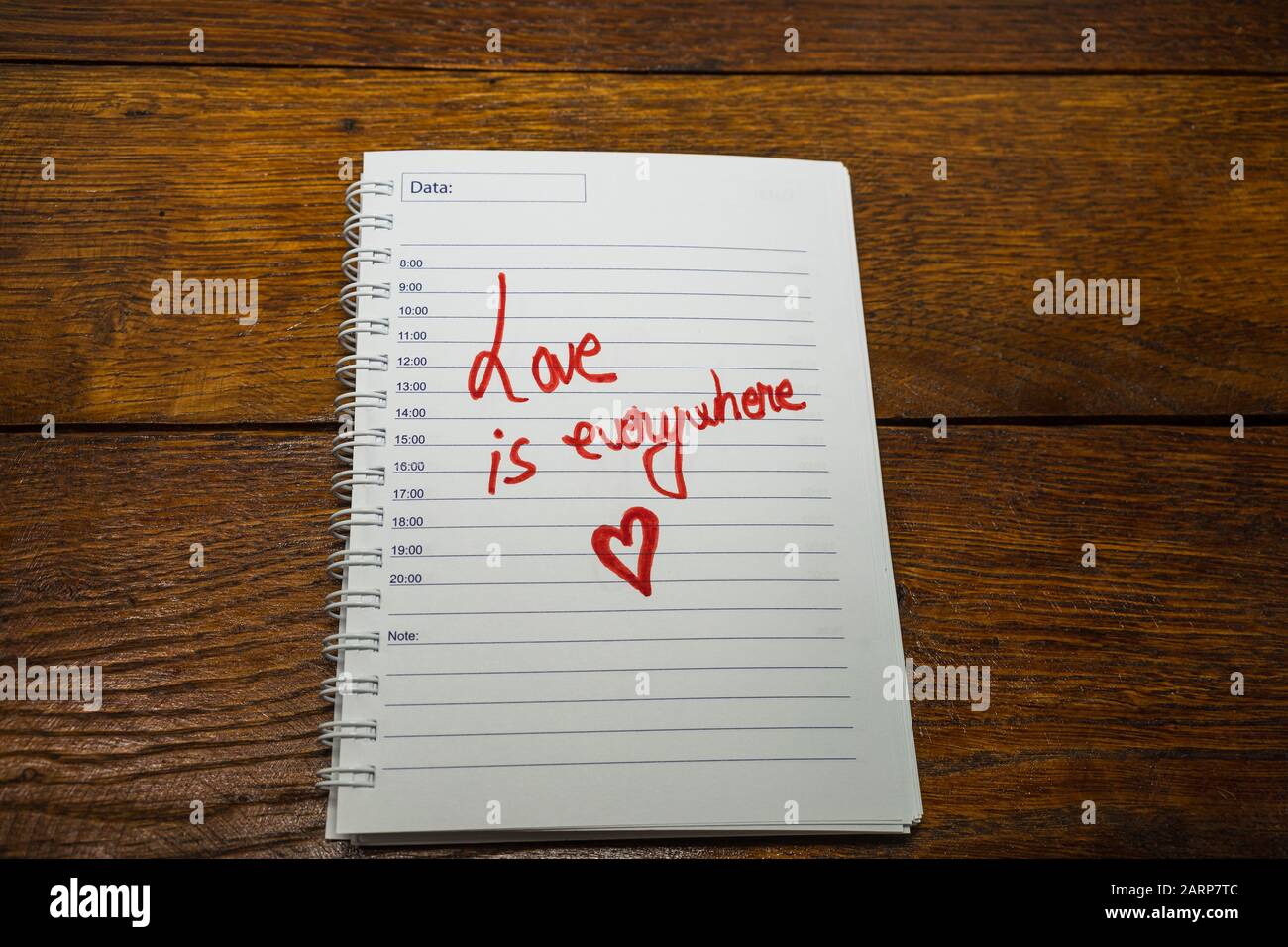 Liebe ist überall und schreibt Liebestext auf Papier, schöne Botschaft. Text auf der Spiralagenda. Romantisches Liebeskonzept. Valentinstag. Stockfoto
