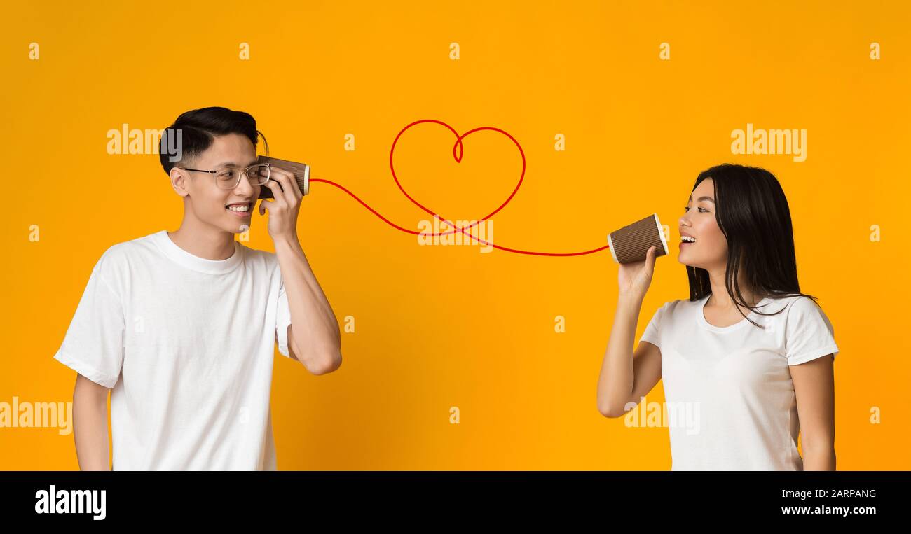 junges asiatisches Paar mit CAN-Telefon auf orangefarbenem Hintergrund Stockfoto