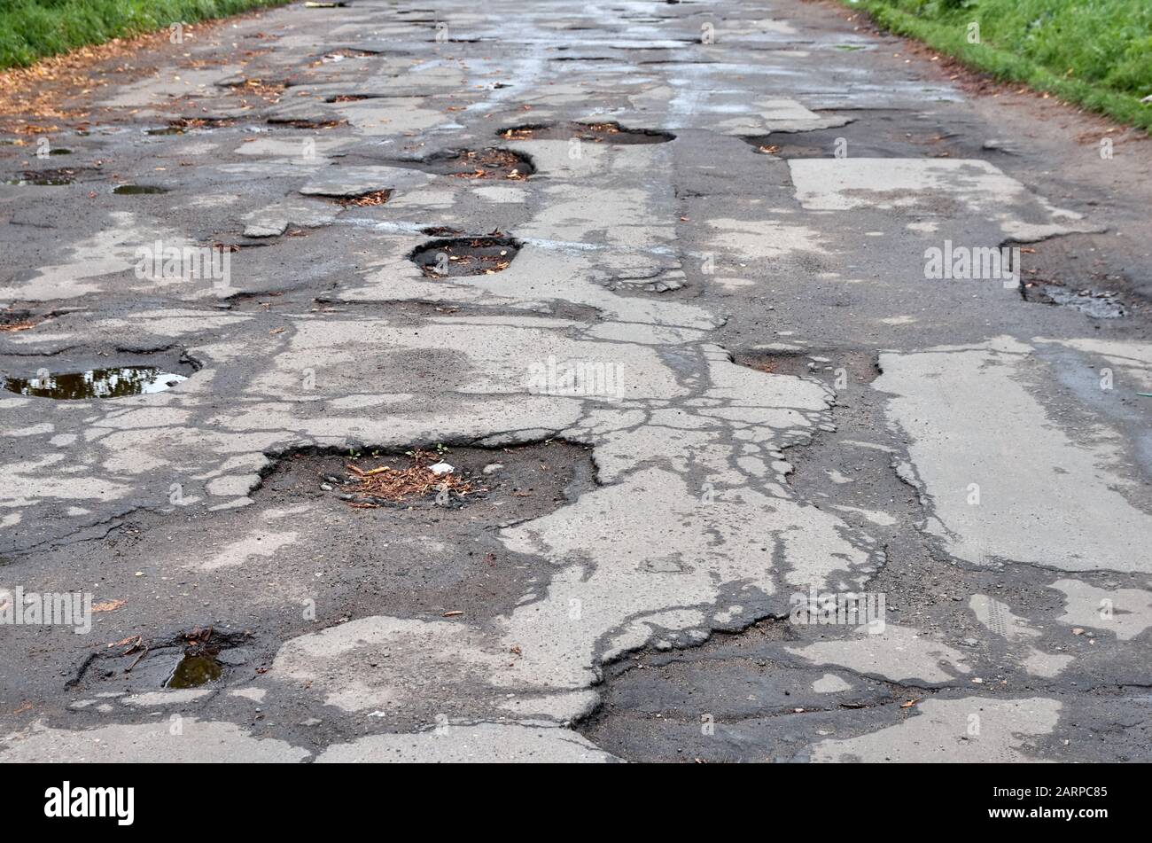 Alte zerstörte Asphaltstraße mit Schlaglöchern und Erschütterungen. Nasse Herbststraße mit Blättern. Stockfoto