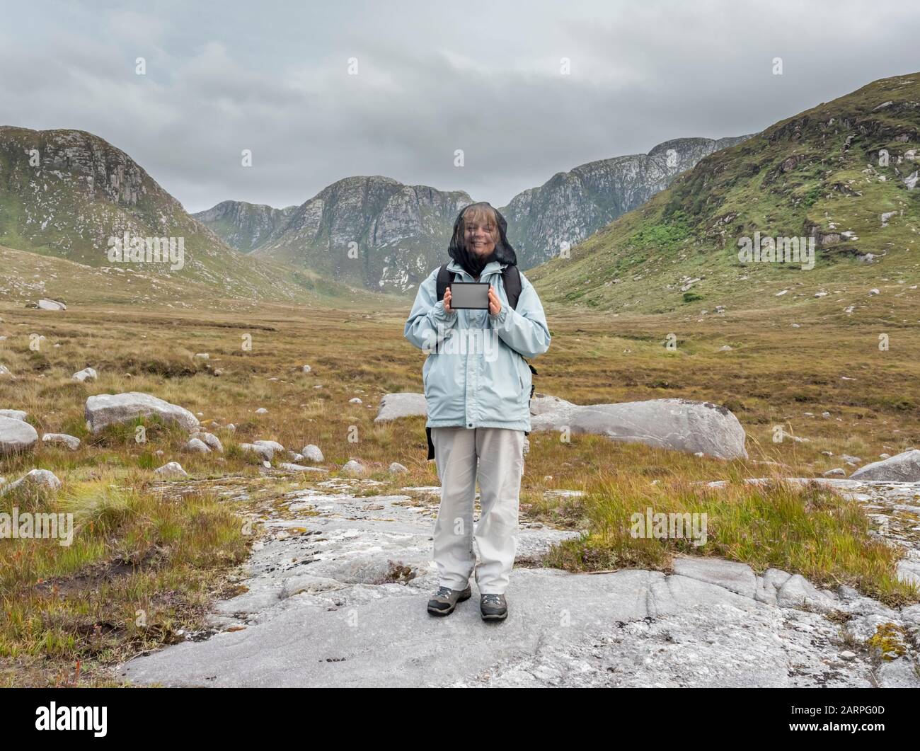 Eine Frau, die ein Netz über ihrem Gesicht trägt, um sich vor Mittelstürzen zu schützen, hält eine graue Karte, um dem Fotografen im Poison Glen, County Donegal, Irland, zu helfen Stockfoto