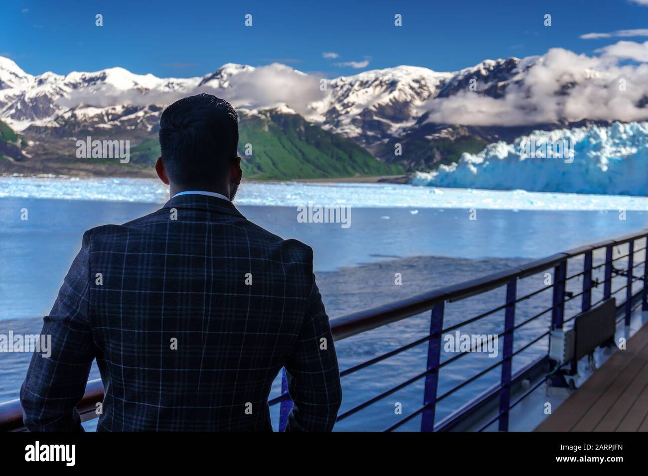 Geschäftsmann in Anzug sucht auf Hubbard-Gletscher. Offenes Deck auf einem Kreuzfahrtschiff und fantastischer Blick auf die Schneehöhe der Berge und weiße Wolken. Stockfoto