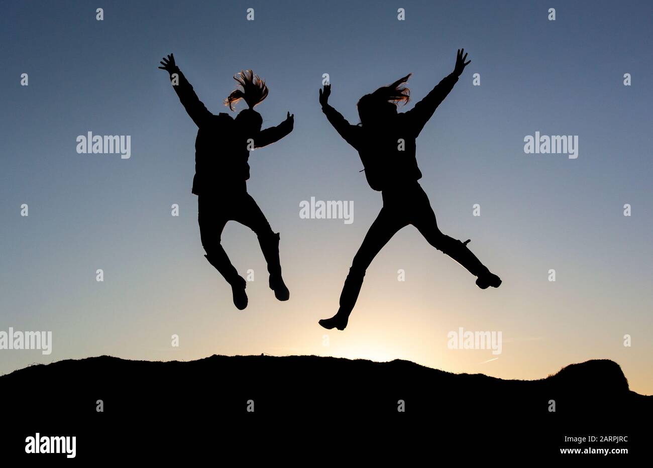 Zwei Teenager-Mädchen springen gegen einen Sonnenaufgang. North Yorkshire, Großbritannien. Stockfoto