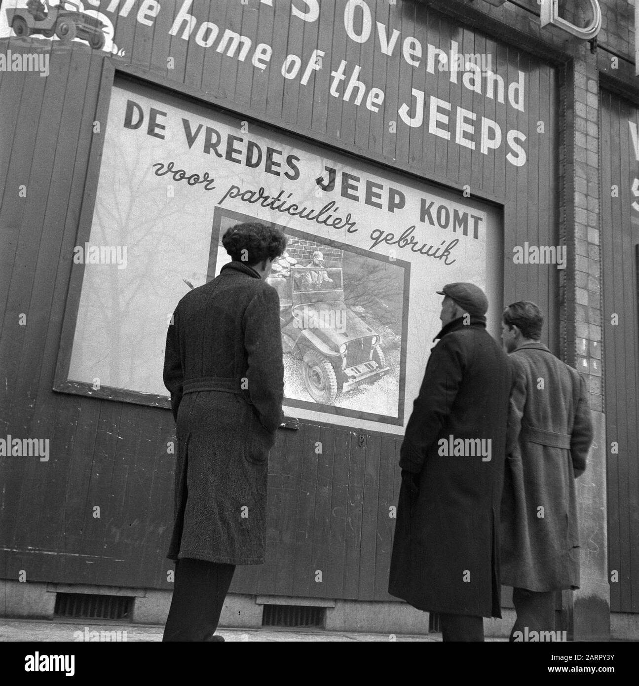 Passanten sehen ein Plakat mit dem Text De Vredes Jeep Comes Date: 12. Dezember 1945 Schlagwörter: Plakate, Plakate Stockfoto