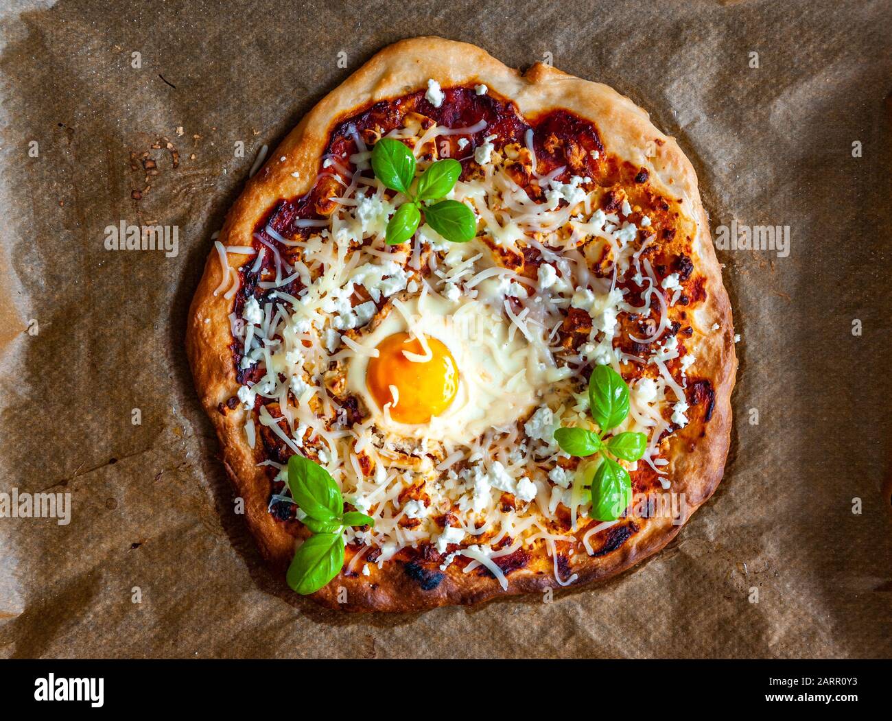 Obenliegender Schuss einer Pizza mit Ei, Käse und Kräutern. Rustikale Szene und dramatisches Licht. Stockfoto