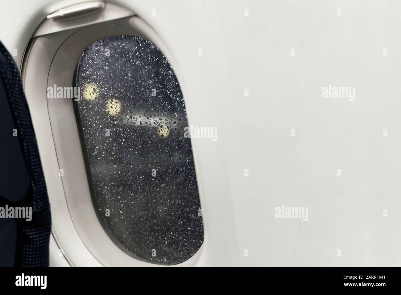 Nachtansicht von der Flugzeugbeleuchtung auf den Flughafenleuchten. Regenstreuung auf dem Porthole-Glas aufgrund von schlechtem Regenwetter. Flugzeug bringt Sie zu Stockfoto