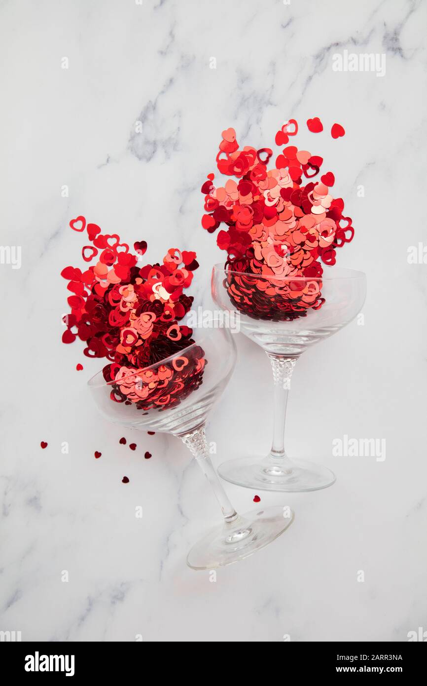 Champagnerglas überströmt mit rotem Valentinskerz Herzconfetti Stockfoto