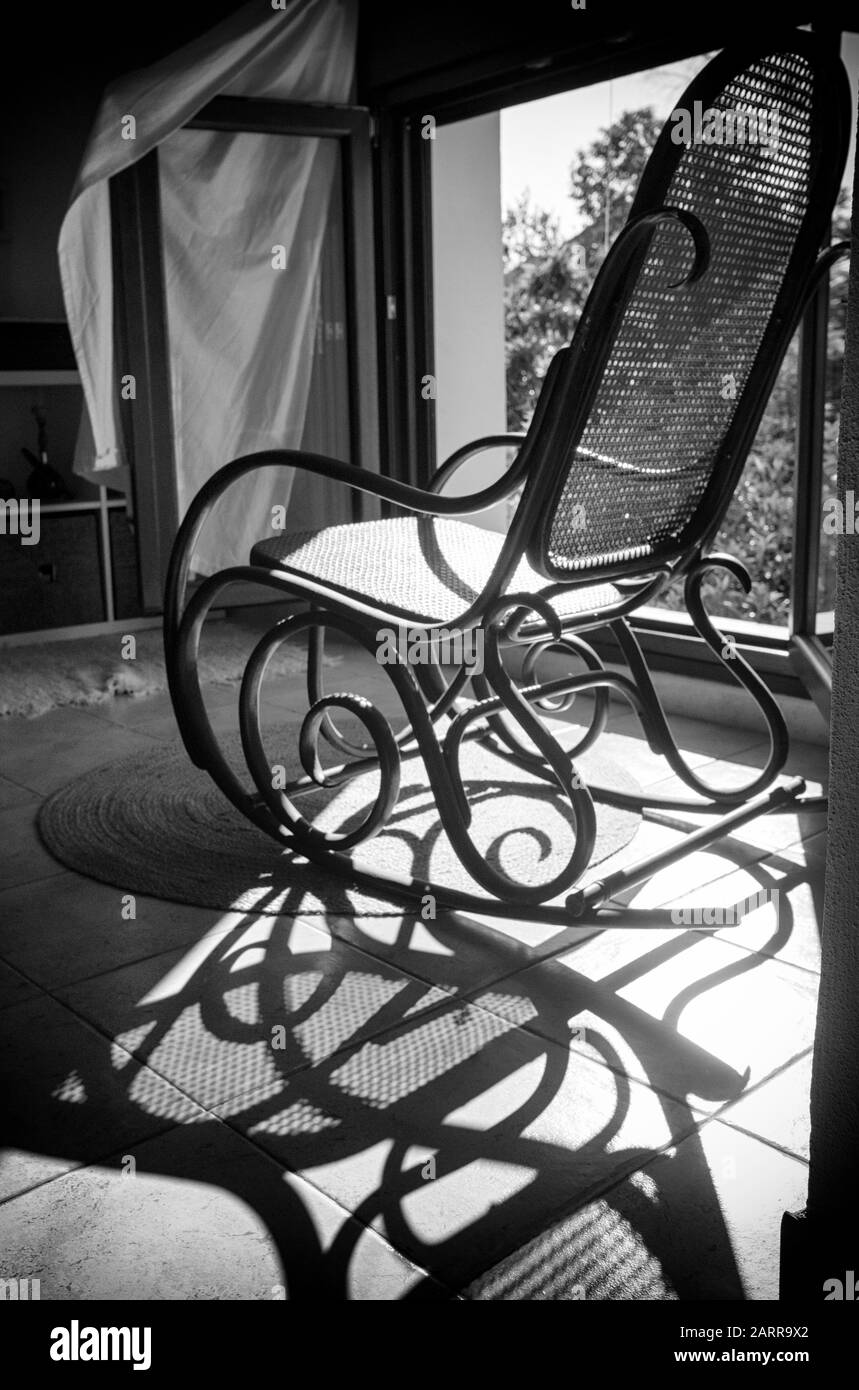 Vintage-Schaukelstuhl und sein Schatten, der vom Sonnenlicht kommt, das durch das nahe gelegene Fenster kommt. Vintage-Möbel. Schwarzweiß, Schwarzweiß, Schwarzweiß, Schwarzweiß Stockfoto