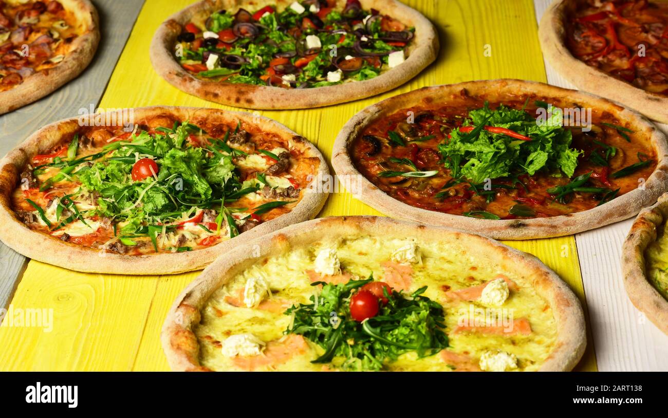 Nehmen Sie Lebensmittel mit verschiedenen Zutaten und knackigen Rändern weg. Fast Food Restaurant Konzept. Pizza kreist mit Fleisch, Pilzen, Tomaten und Käse auf gelbem Holzhintergrund. Verschiedene Pizza für die Speisekarte Stockfoto