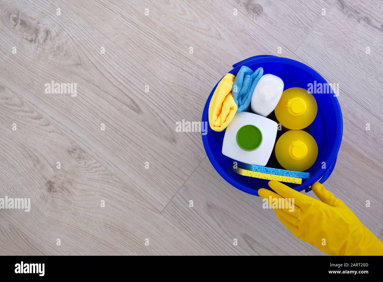 Waschmittel in Kunststoffflaschen, Schwämmen, Bürsten in blauem Haushaltsbehälter mit Kopierraum. Hand in gelben Gummihandschuh auf hellem Holzhintergrund, oben VI Stockfoto Waschmittel in Kunststoffflaschen, Schwämmen, Bürsten in blauem Haushaltsbehälter mit Kopierraum. Hand in gelben Gummihandschuh auf hellem Holzhintergrund, oben VI Stockfoto