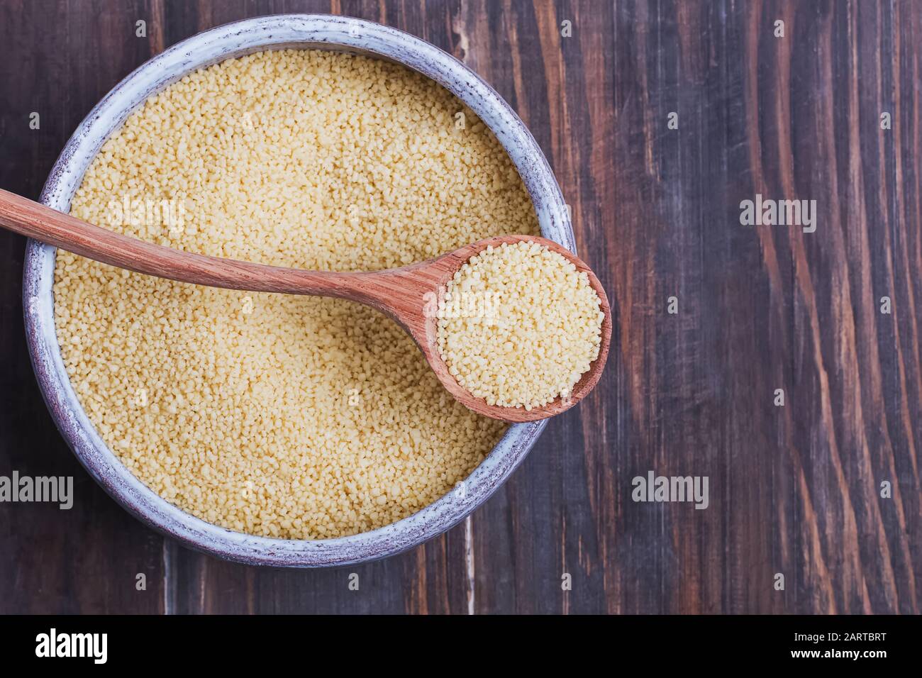 Trockenes Couscous in einer Schüssel und Löffel auf Holzgrund, Stockfoto