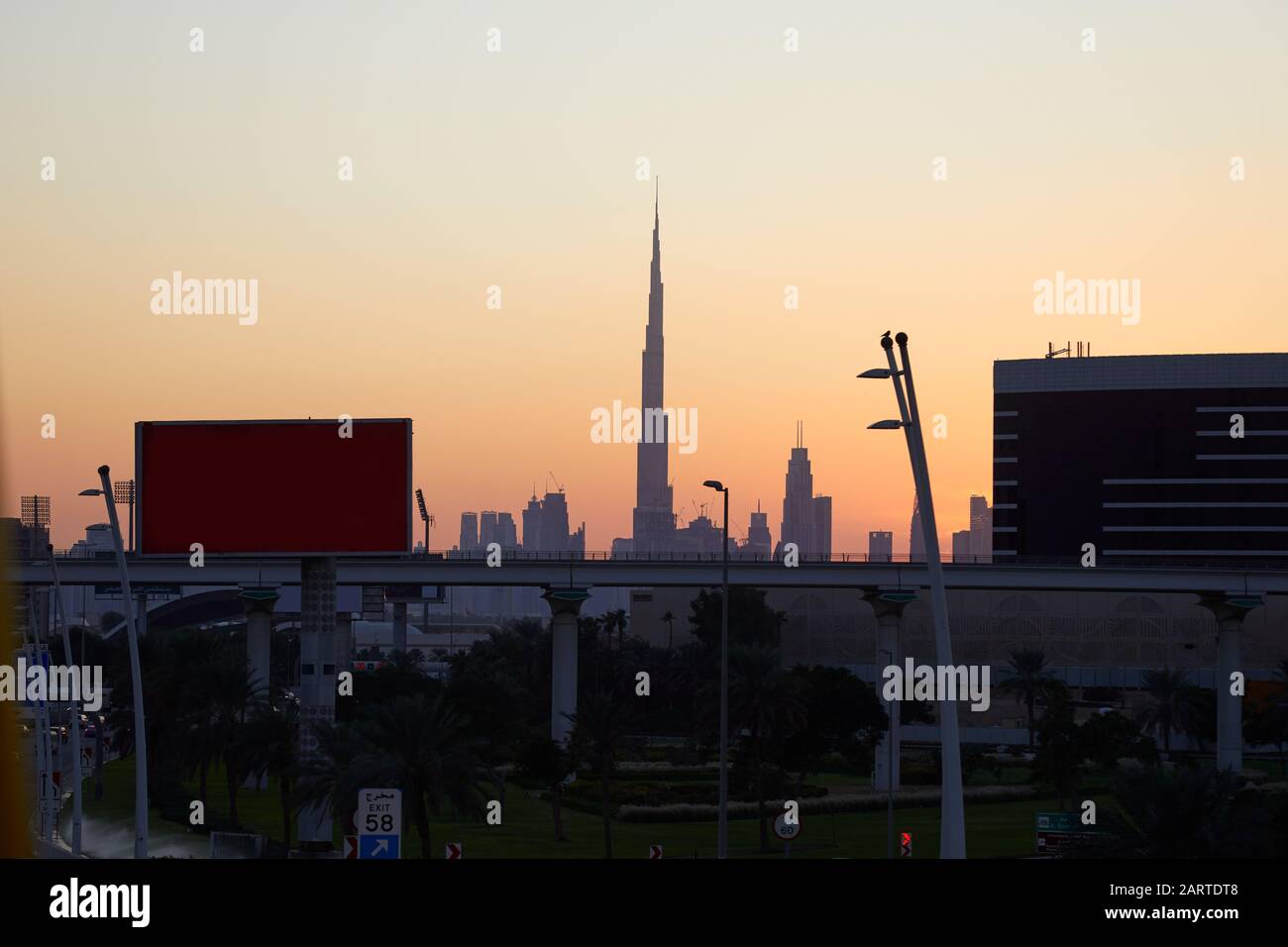 Skyline von Dubai mit dem Wolkenkratzer Burj Khalifa bei Sonnenuntergang, klarem Himmel mit Überführung, Plakaten und Straße in den Vereinigten Arabischen Emiraten Stockfoto