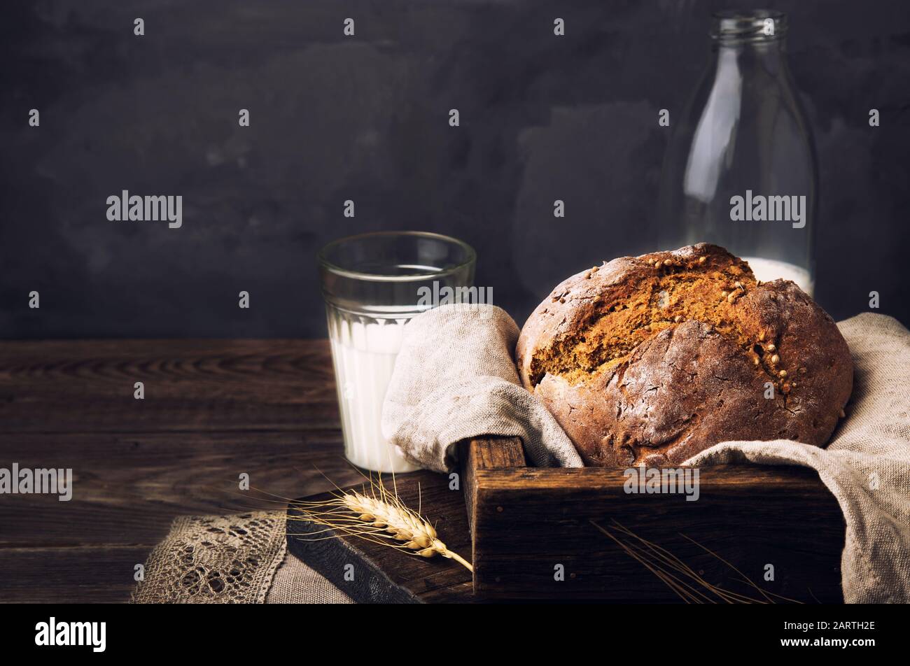 Hausgemachtes Roggenbrot mit Koriandersamen und einer Flasche Milch auf altem Holztisch. Ländliches Essen Stillleben. Stockfoto