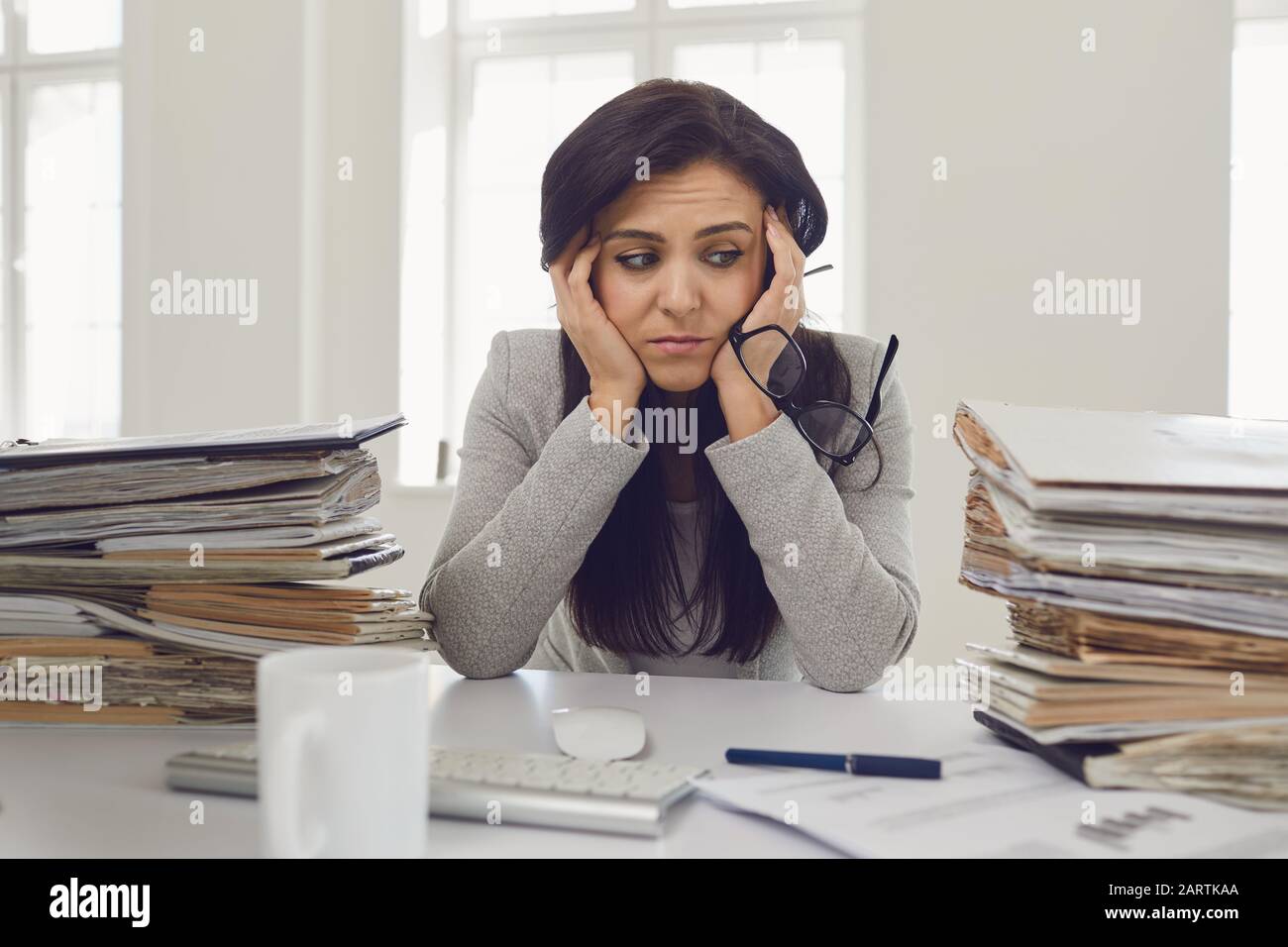 Frau brünette Geschäftsfrau in Brille mit einem Berg von Dokumenten auf dem Tisch müde depressiv empfindet enttäuscht depressiv am Tisch in Stockfoto