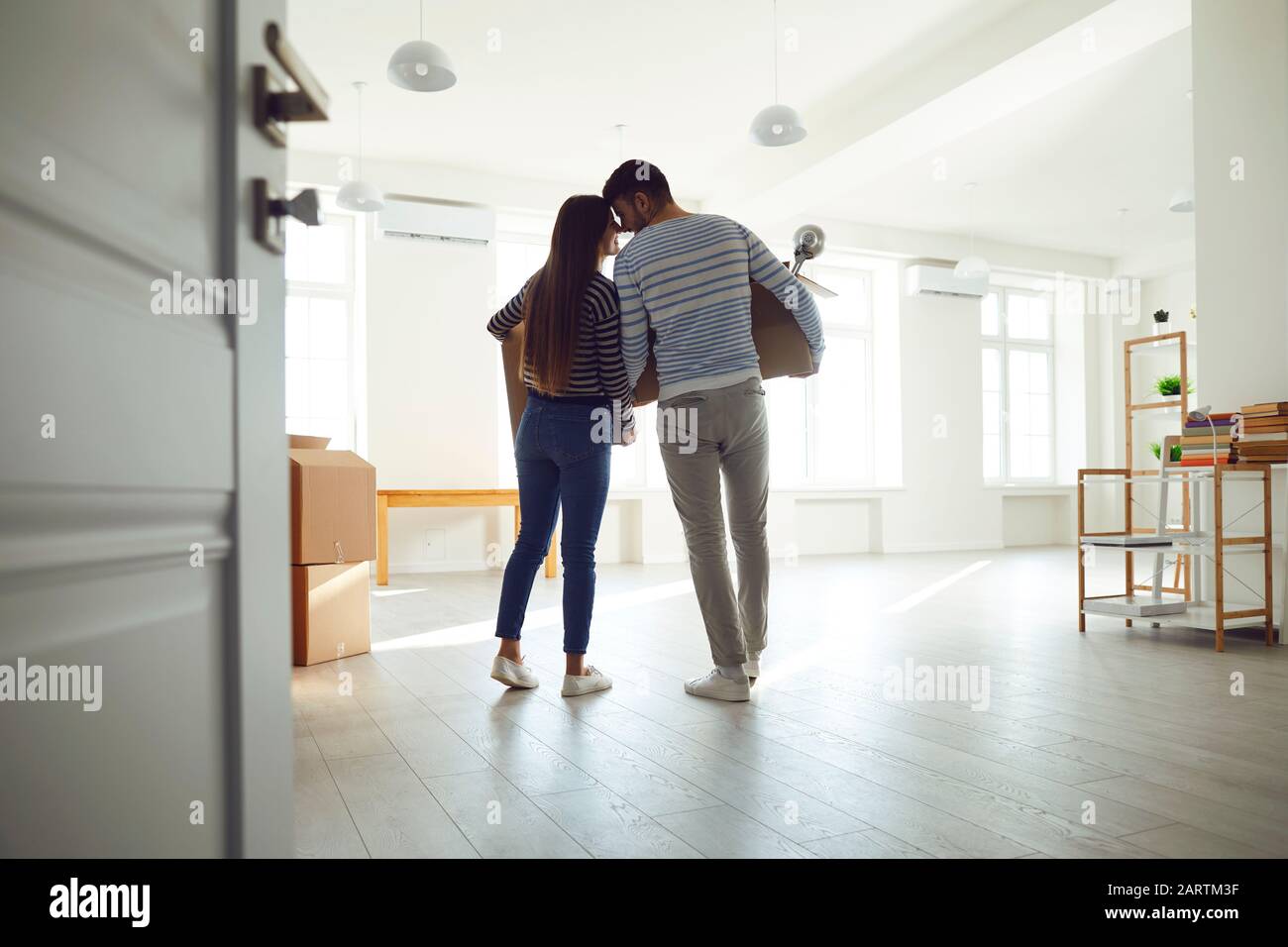 Rückansicht in Bewegung. Junge Paar-Familie mit Kisten, die in einem neuen Hausraum umziehen sollen. Stockfoto