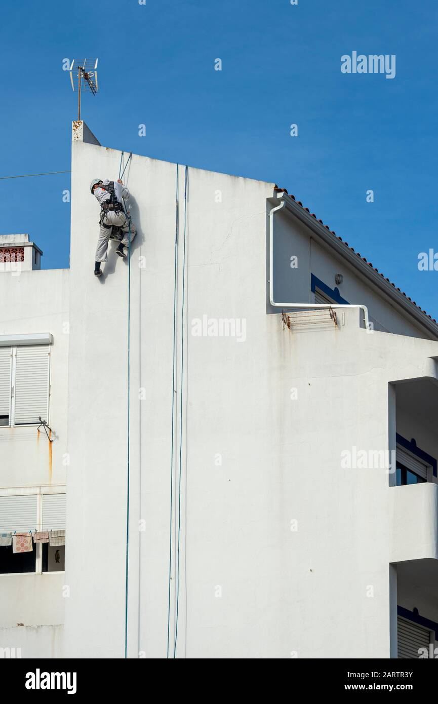 Seilzugangsabseiler, Gebäudereparaturen und Maler tragen an der Seite eines Gebäudes einen vollen Sicherheitskabelbaum Stockfoto