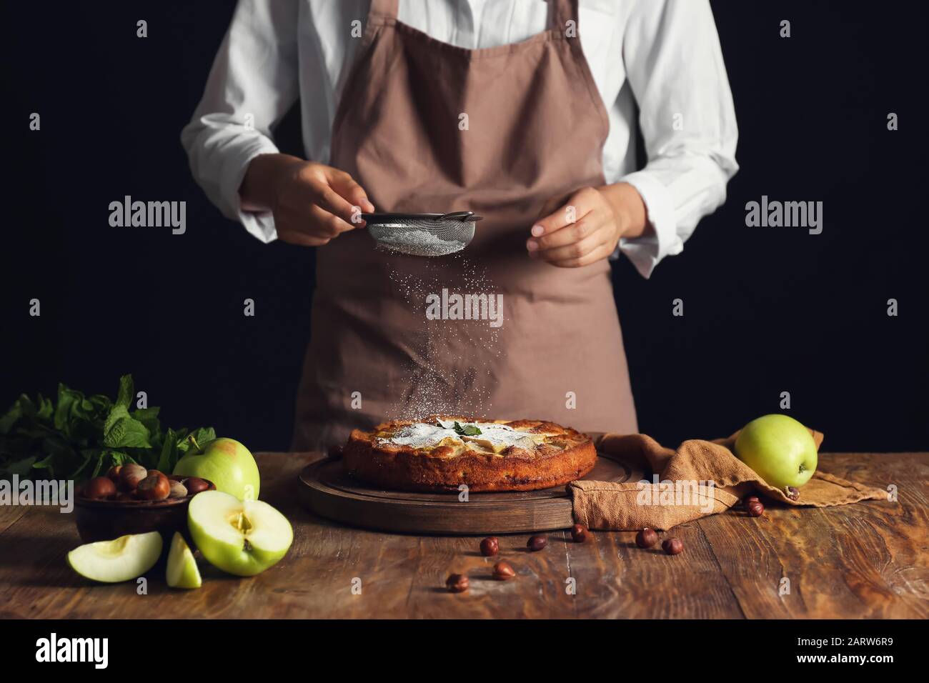 Frau streut Zuckerpulver auf apfelkuchen auf den Tisch Stockfoto