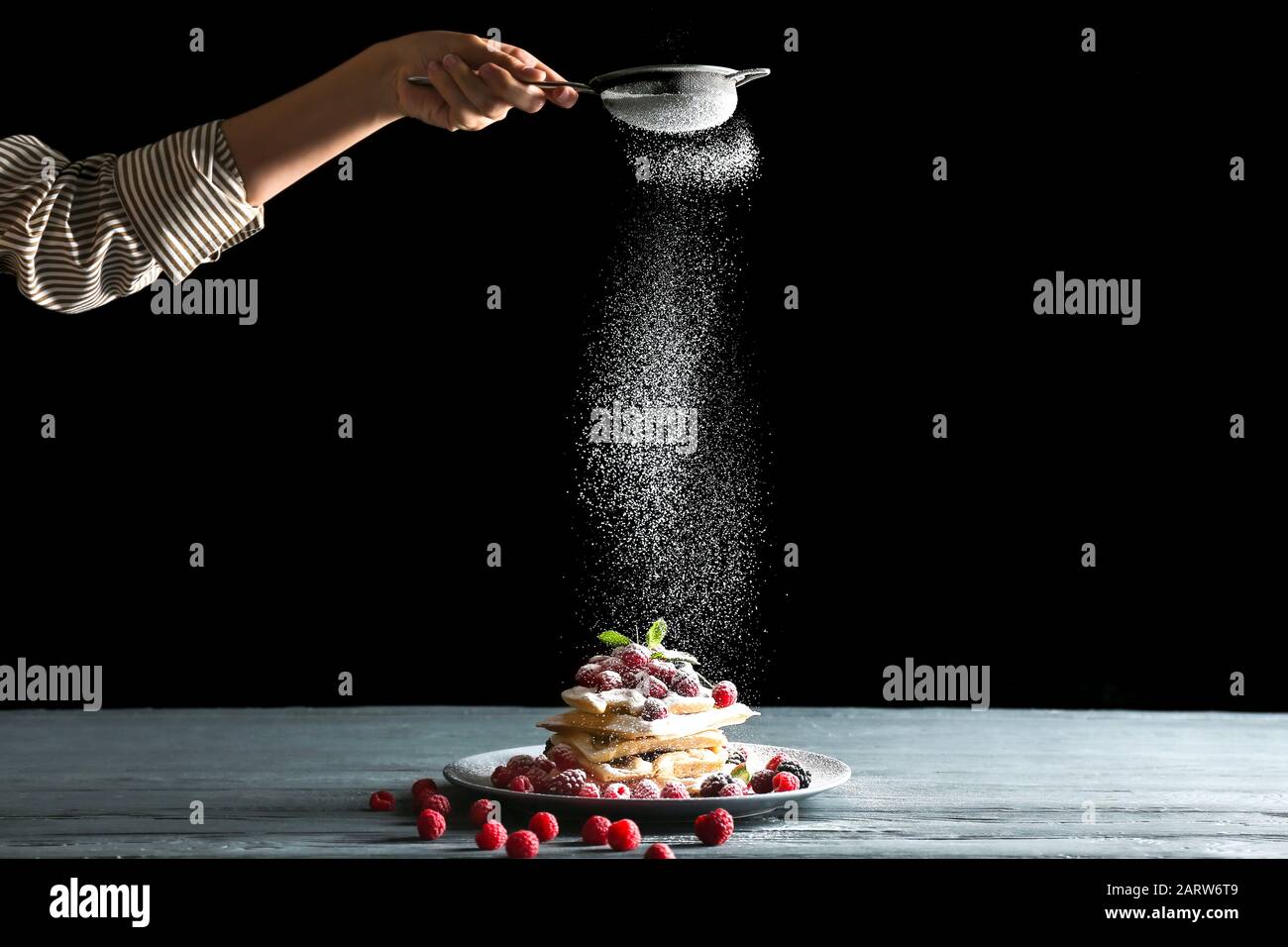Frau streut Zuckerpulver auf belgische Wafer auf den Tisch Stockfoto